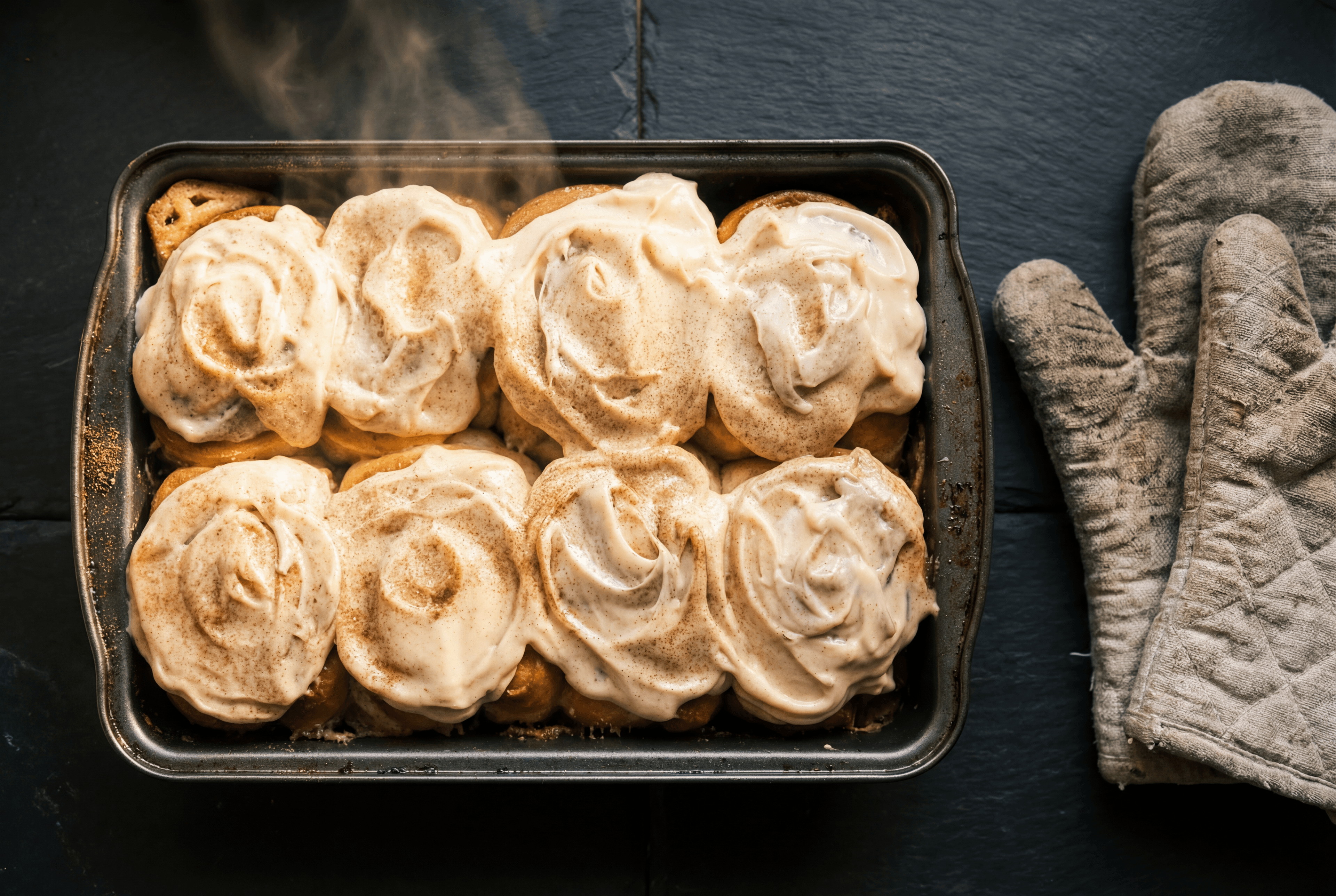 Overhead shot of six golden cinnamon rolls in a seasoned baking tin with steam rising